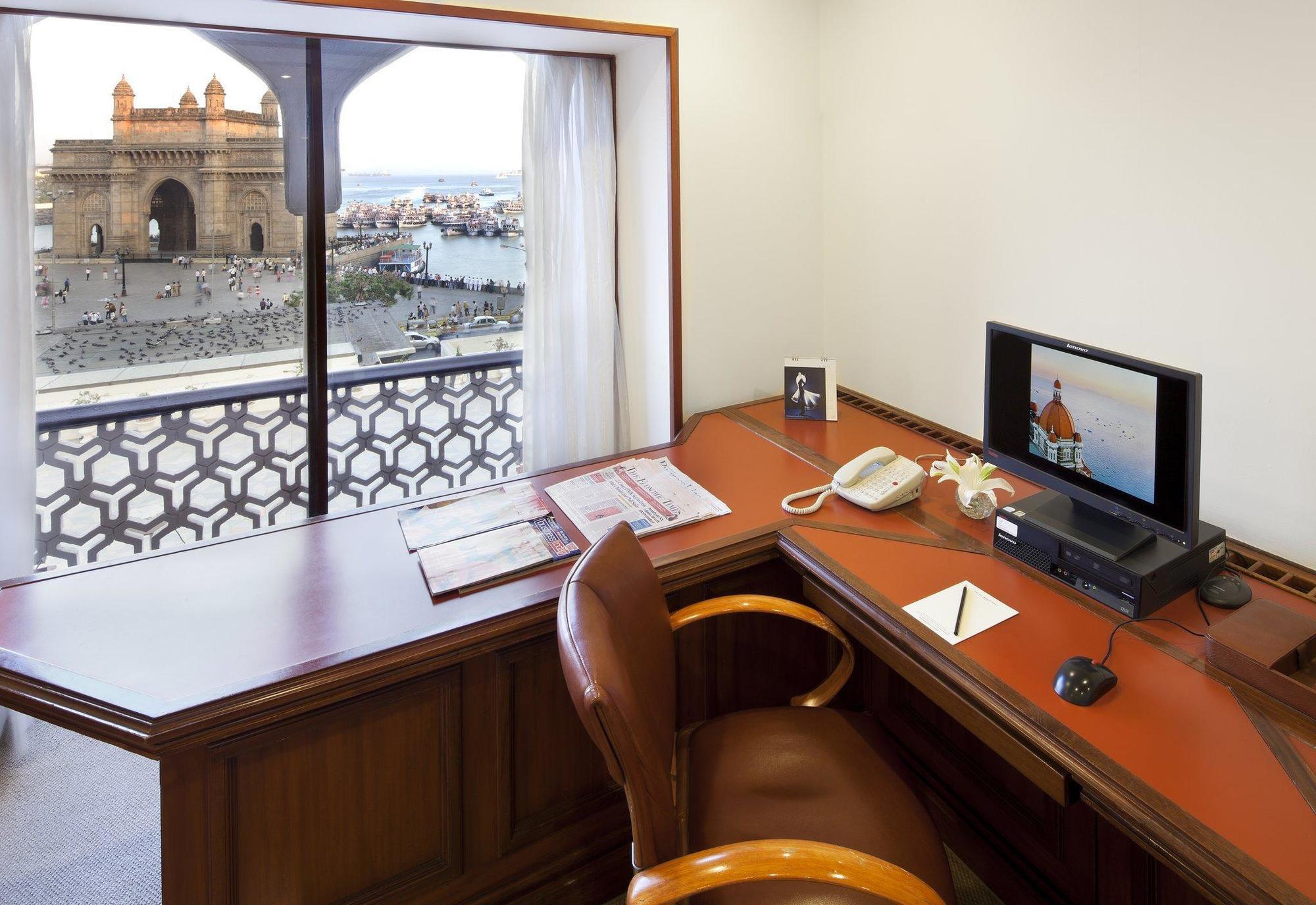 The Taj Mahal Tower, Mumbai Ξενοδοχείο Εξωτερικό φωτογραφία The photo shows a workspace with a wooden desk and an ergonomic chair. On the desk, there is a computer monitor, a telephone, and some stationery items. A window provides a view of an outdoor scene, possibly featuring water and structures or building