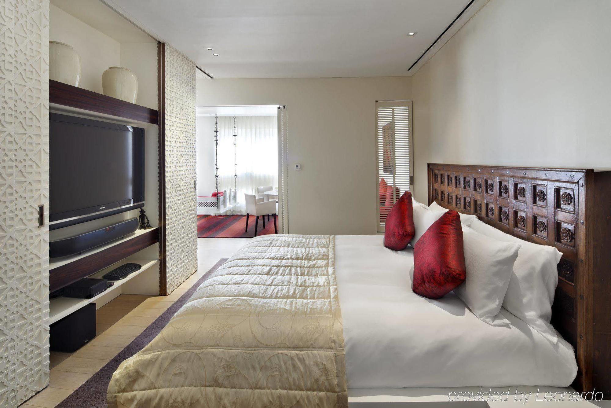 The Taj Mahal Tower, Mumbai Ξενοδοχείο Εξωτερικό φωτογραφία The photo depicts a modern hotel bedroom. The room features a large bed with white bedding and decorative red pillows. A beautifully carved wooden headboard adds an elegant touch. In the background, there is a flat-screen TV mounted on the wall, alon