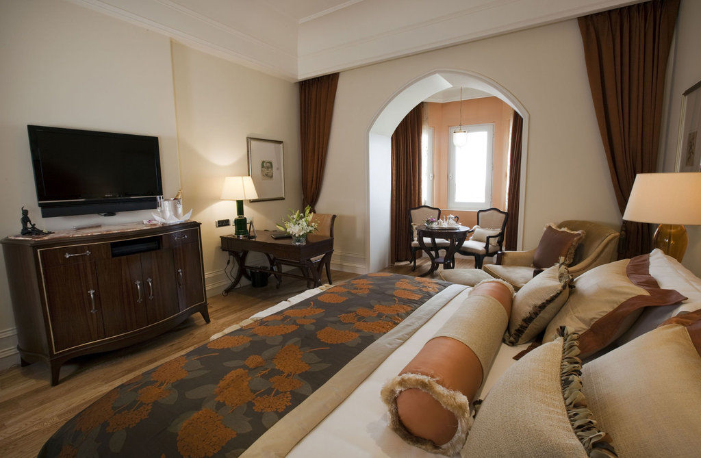 The Taj Mahal Tower, Mumbai Ξενοδοχείο Εξωτερικό φωτογραφία The photo shows a beautifully arranged hotel room featuring a king-size bed with decorative pillows and a stylish bedspread. Beside the bed is a modern wooden dresser with a flat-screen TV mounted on the wall. There is a cozy seating area with two ch